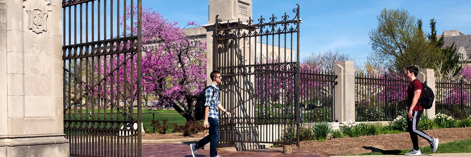 A student walks past gates in the Arboretum at IU Bloomington on a sunny spring day.